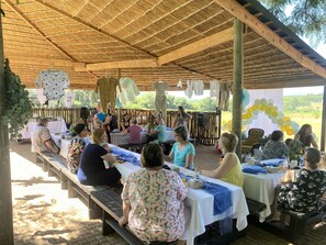 An outdoor event with tables and benches under a thatched roof. - El Roi Guest Lodge (Mbombela)
