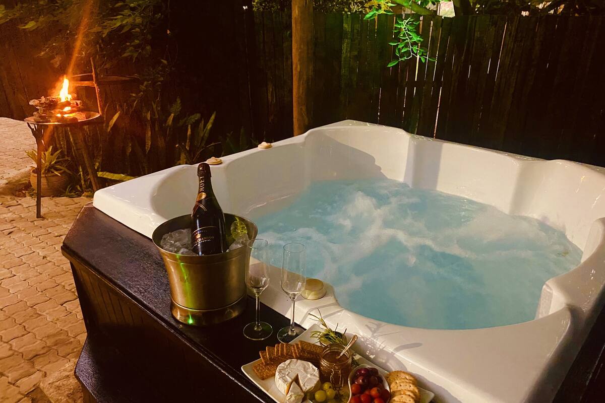 Ein Whirlpool voller Wasser, umgeben von einer Terrasse mit einer Champagnerflasche, Gläsern und einer Platte mit Snacks.