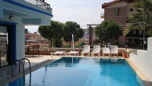 A swimming pool with white lounge chairs and a view of buildings in the background. - Sun Hotel (Cesme)