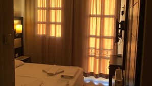 A hotel room with a bed, curtains, a desk, and a lamp. - Sun Hotel (Cesme)