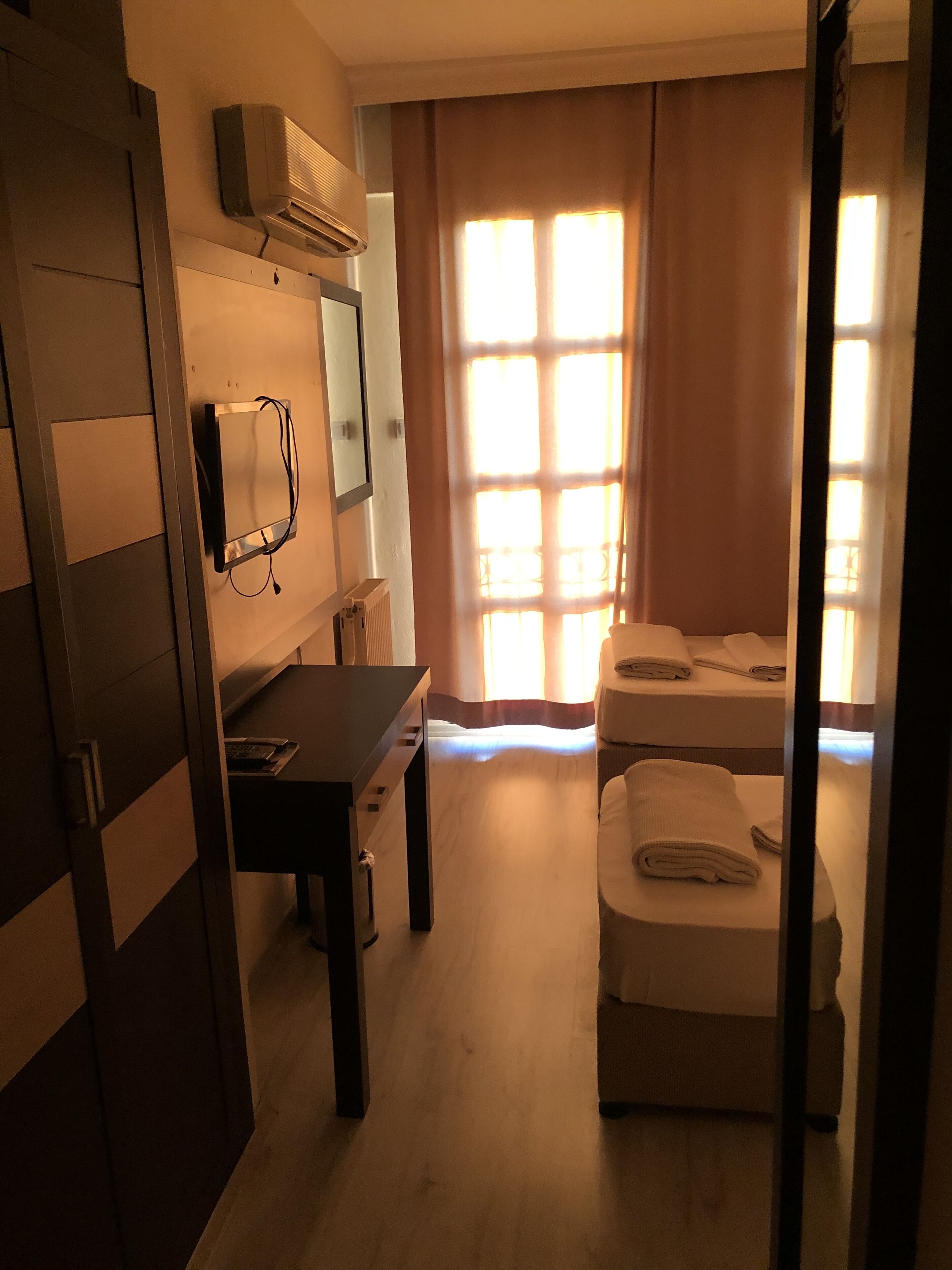 Une chambre d’hôtel avec un plancher en bois, un bureau avec un ordinateur, un lit et une fenêtre avec des rideaux.