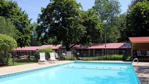 A swimming pool with lounge chairs and a covered area with a red roof. - Luzerne Court Motel (Lake Luzerne)