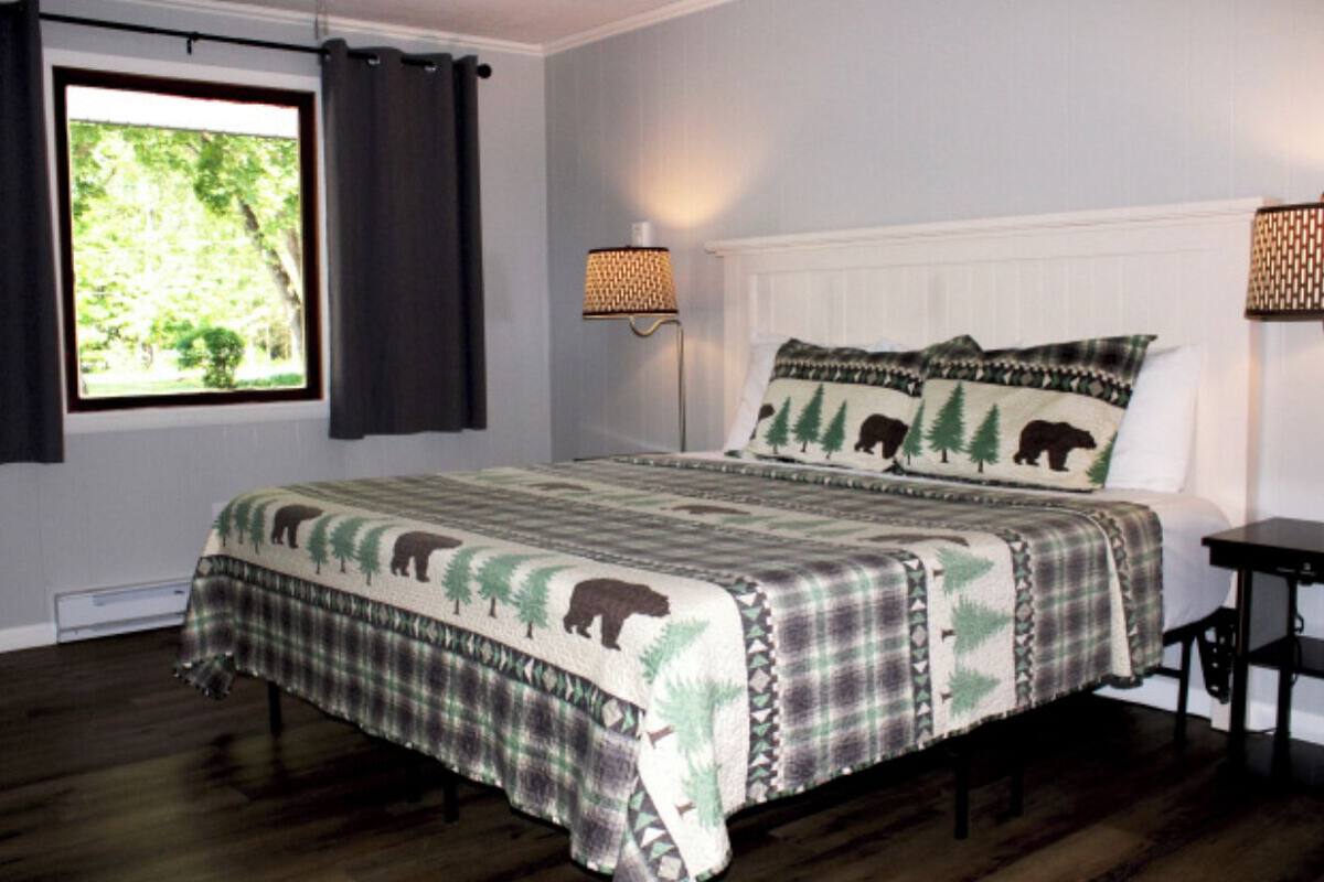 A bedroom with a large bed, dark wooden flooring, a window with curtains, and two wall-mounted lamps.