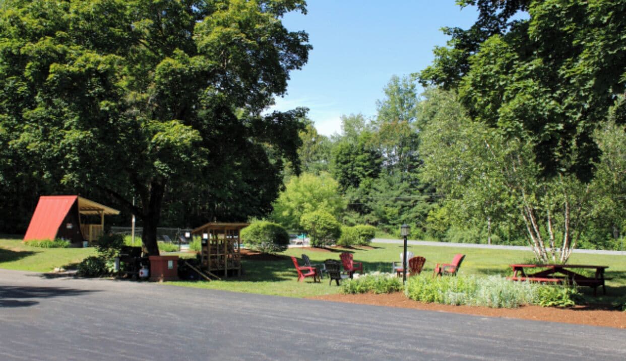 A park with picnic tables and chairs, a covered area, and a road.