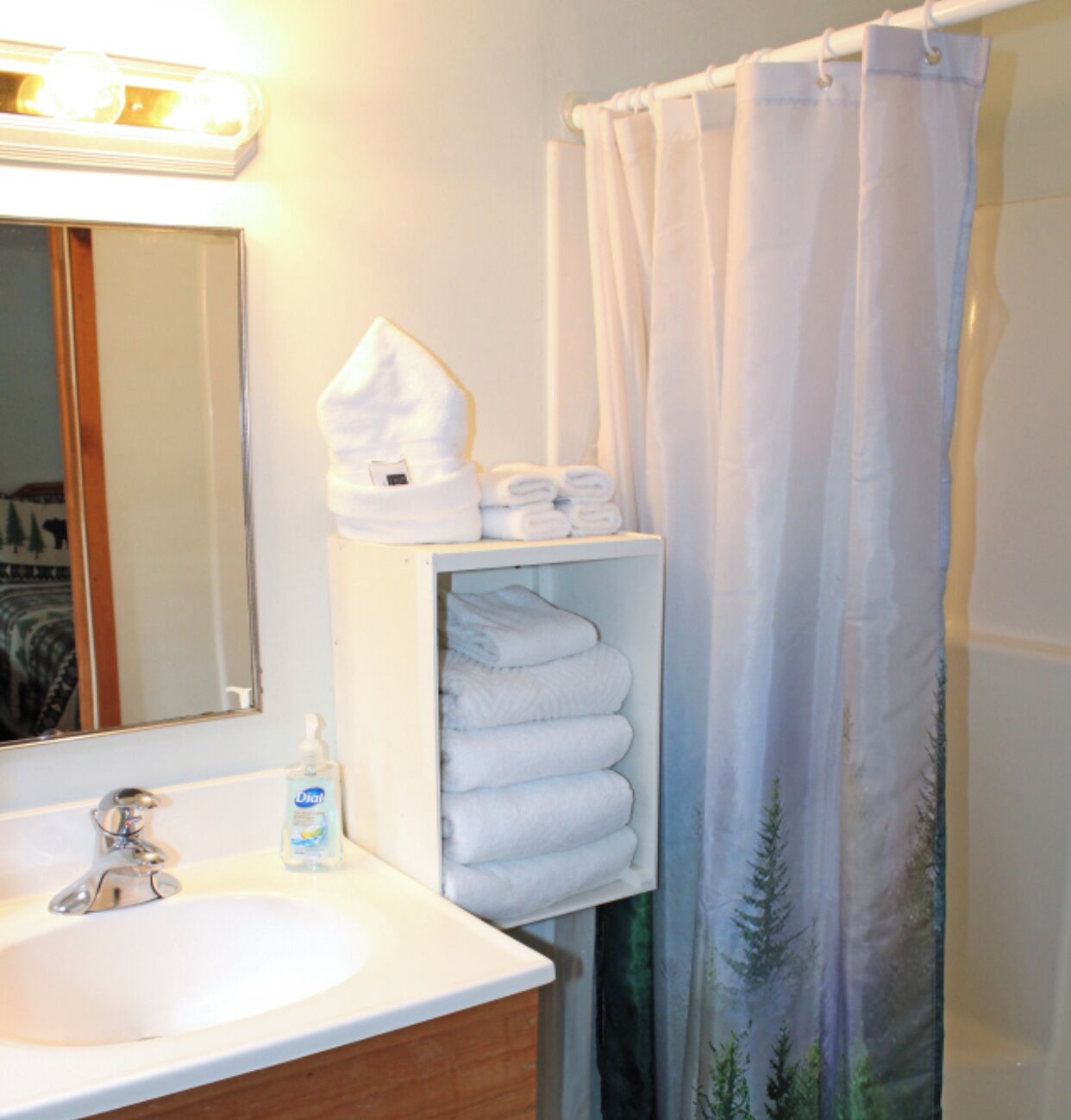 A bathroom with a white sink, a mirror, a shelf with folded towels, and a shower curtain.
