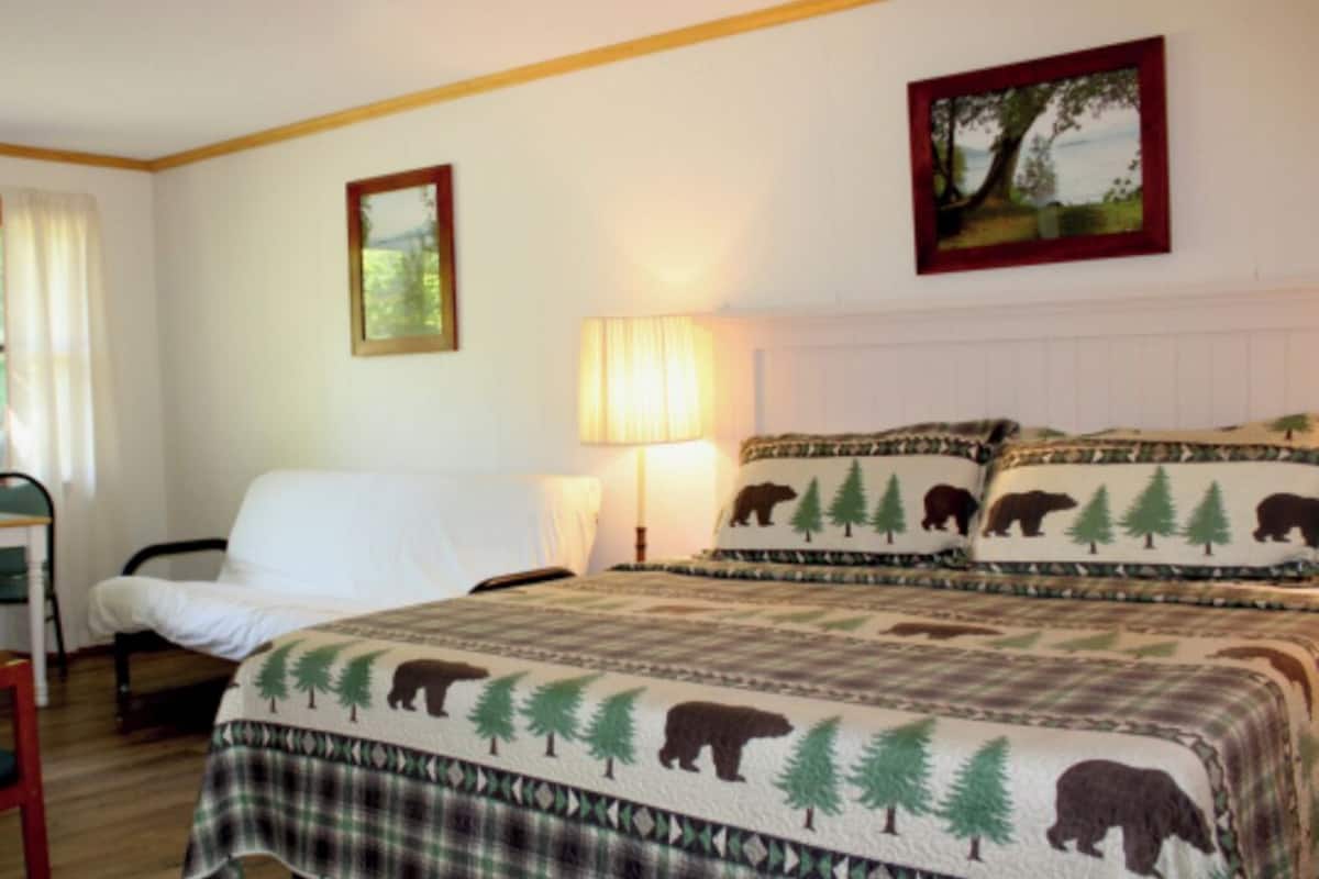 A hotel room with a bed, a desk, a chair, a lamp, and a window with curtains.