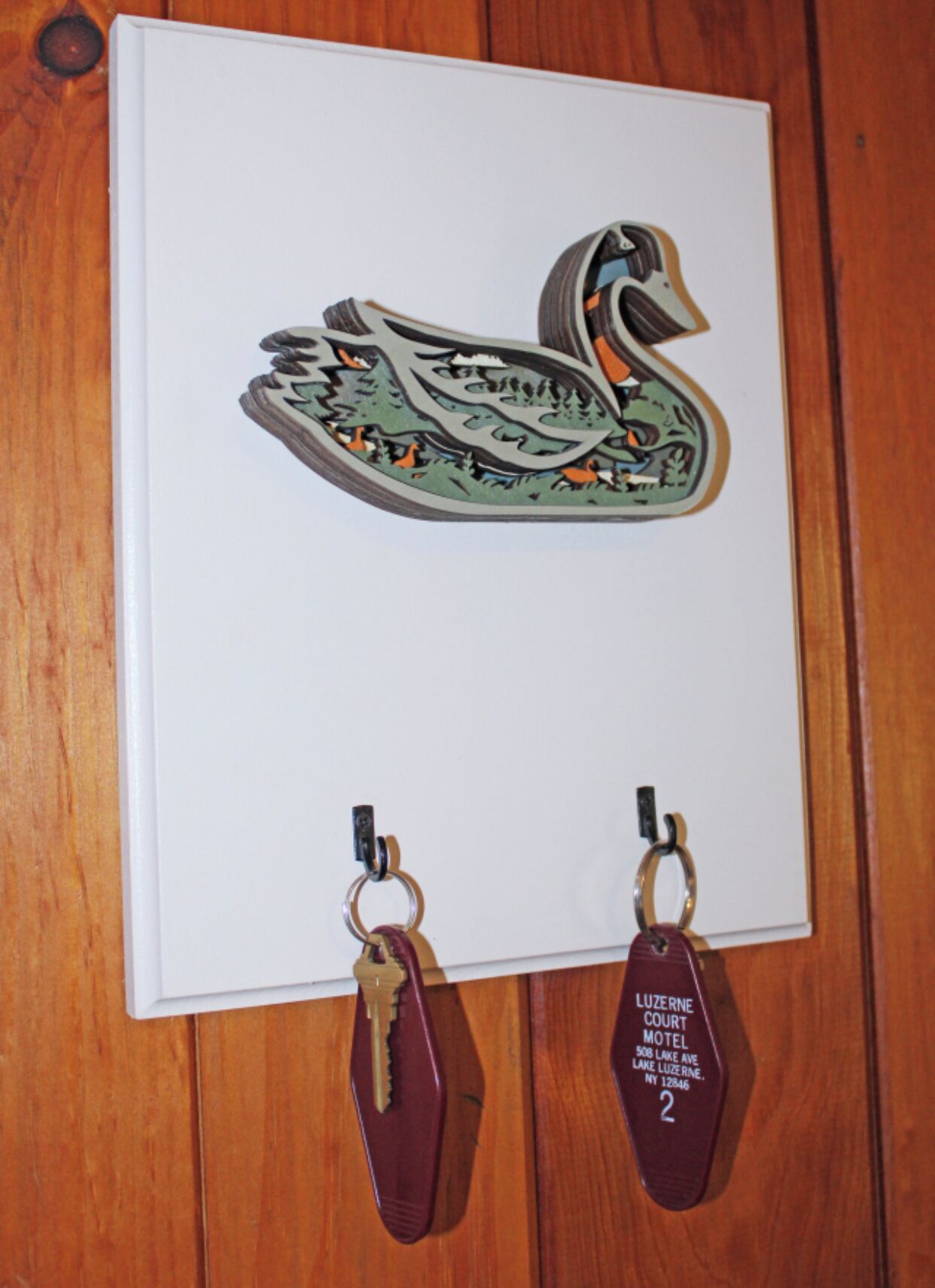 Un porte-clés orné d’un motif de cygne et d’une plaque portant l’inscription : « LUZERNE COURT MOTEL 508 LAKE AVE LUZERNE, NY 12846 ».