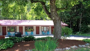 A lodge with a red roof, multiple windows, and a porch with blue chairs. - Luzerne Court Motel (Lake Luzerne)