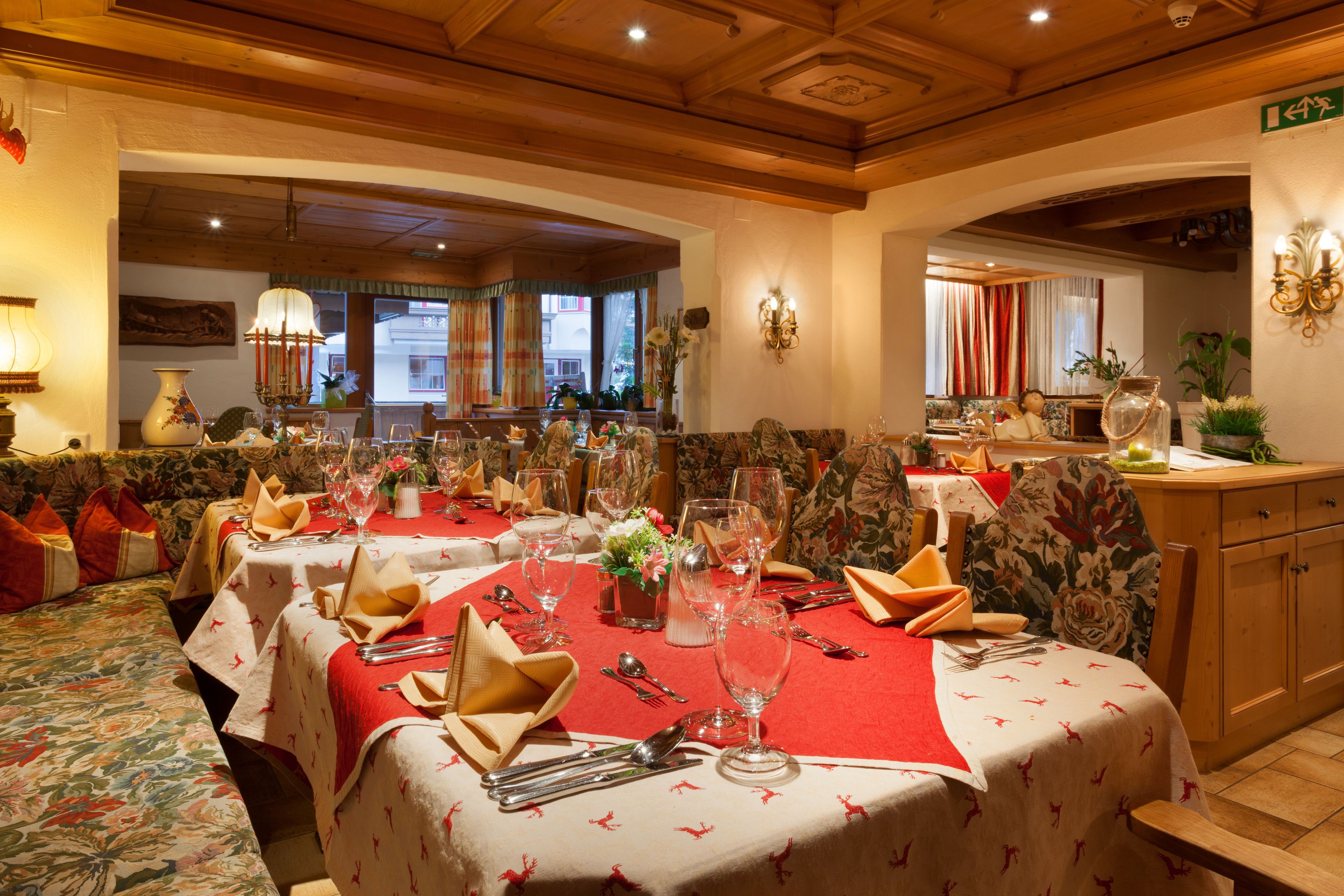 A dining area with tables set for a meal, featuring red tablecloths and floral patterns.