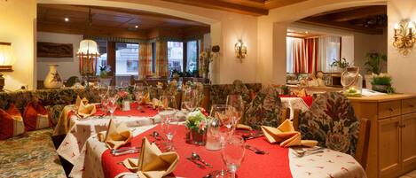 Un comedor con mesas dispuestas para una comida, con manteles rojos y estampados florales.