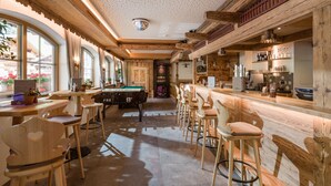 A bar area with a pool table, bar stools, and a wooden ceiling with exposed beams. - Hotel Pinzger (Tux)