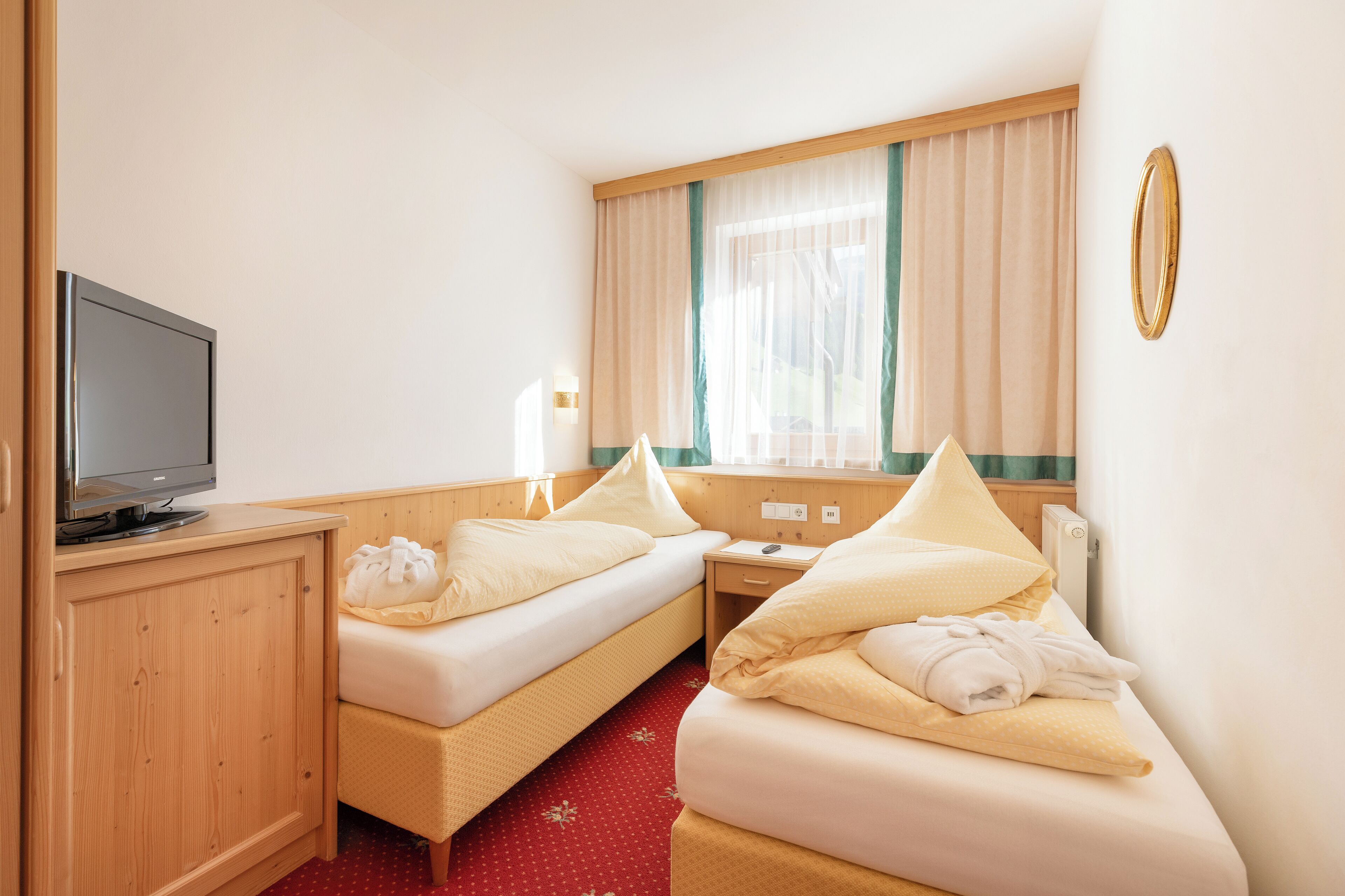 A hotel room with two beds, a television, a wooden cabinet, and a window with curtains.
