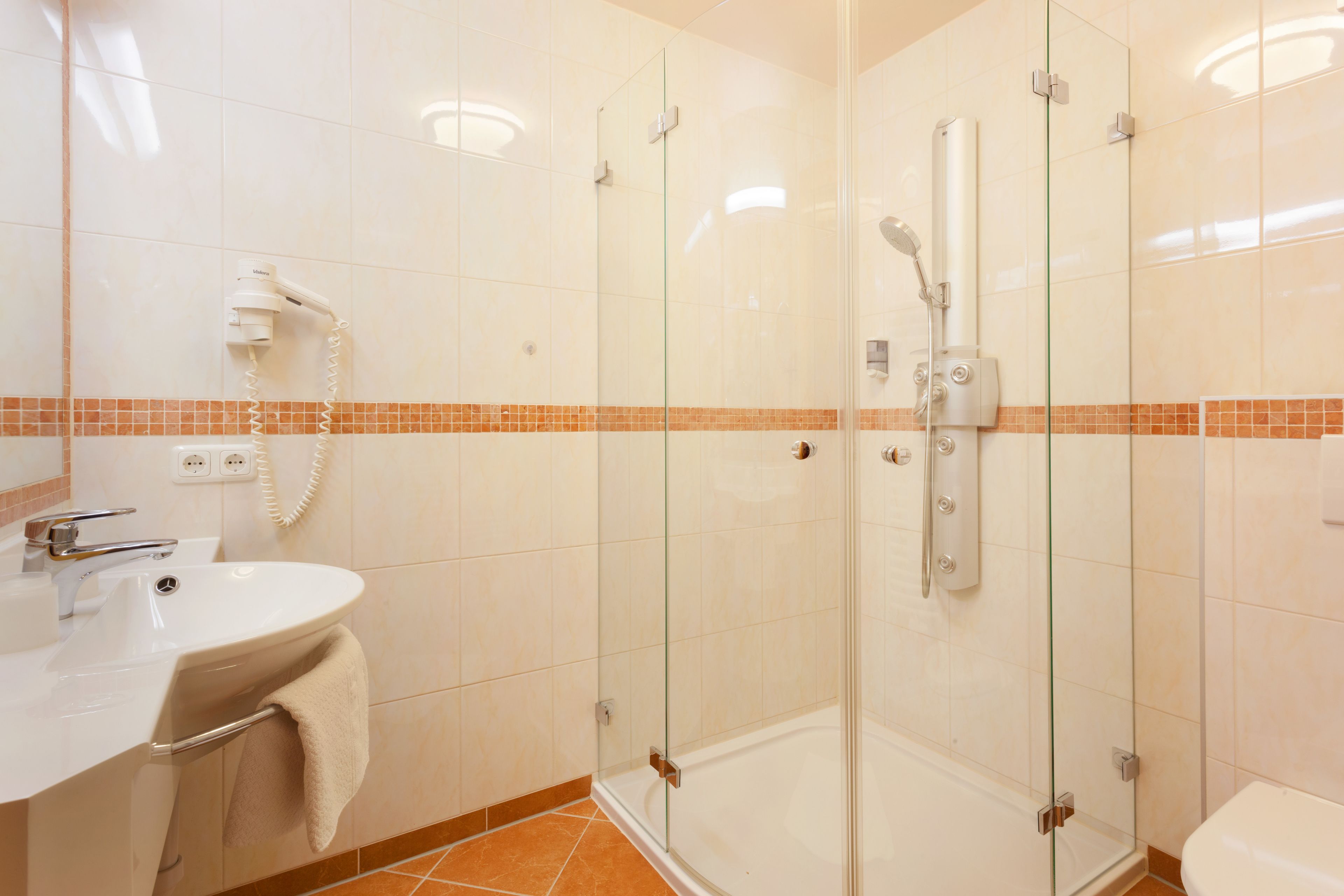 Une salle de bain moderne avec une douche à parois de verre, un lavabo avec une serviette et un sèche-cheveux fixé au mur.