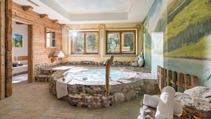 A spa area with a hot tub, stone seating, wooden walls, and a mural of a landscape. - Hotel Pinzger (Tux)