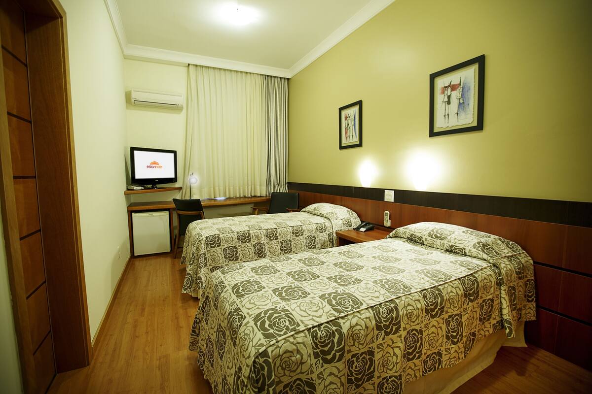 A hotel room with two beds, a desk, a chair, an air conditioning unit, and a television.