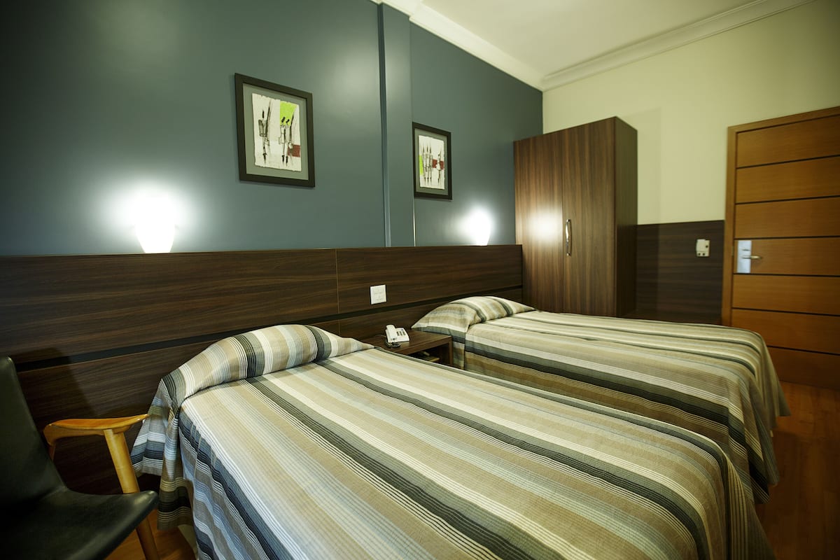 A hotel room with two beds, a wooden wardrobe, and a desk with a telephone.