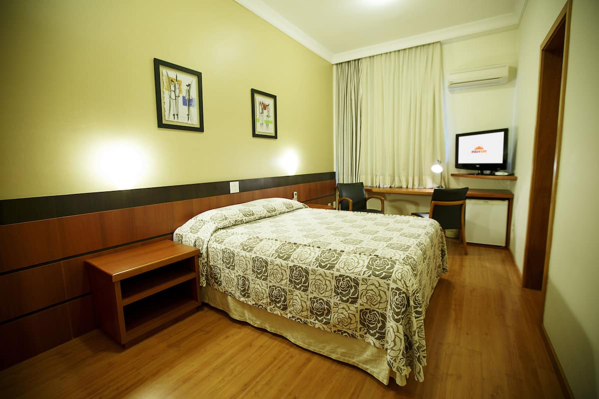 A hotel room with a bed, a desk, a chair, a television, and a window with curtains.