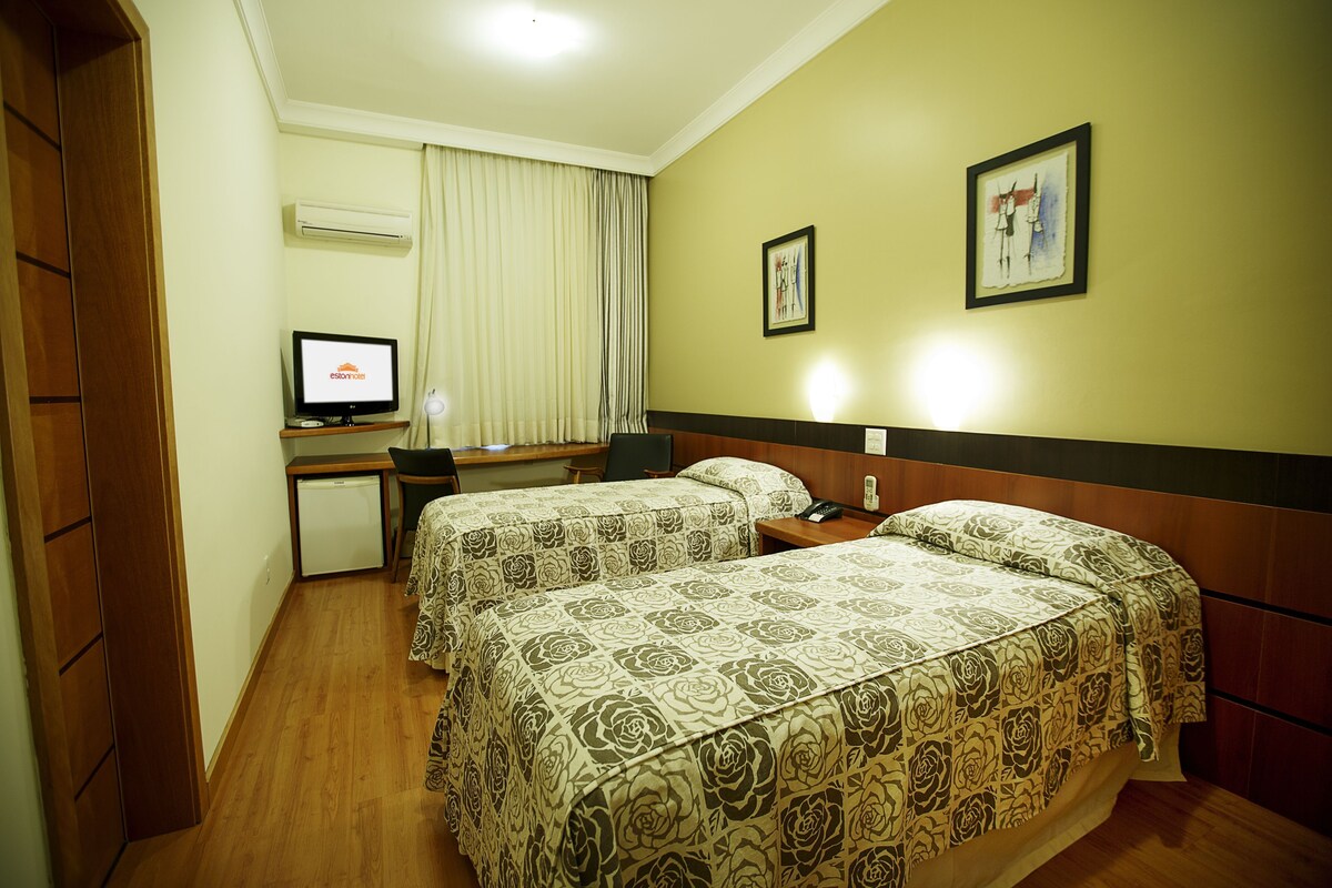 Habitación de hotel con dos camas, un escritorio, una silla, un equipo de aire acondicionado y un televisor.