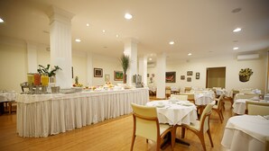 Un grand espace dédié à la salle à manger, avec plusieurs tables et chaises, un buffet et une colonne centrale agrémentée d’une plante.