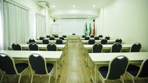 Une salle de conférence avec des rangées de tables et de chaises, des drapeaux et un tableau blanc.