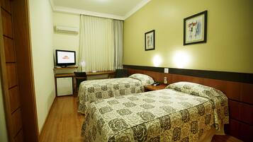 A hotel room with two beds, a desk, a chair, and a television.