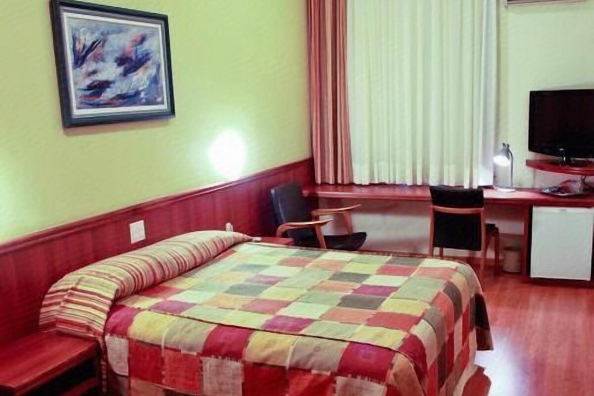 Une chambre d’hôtel équipée d’un lit, d’un bureau, d’une chaise, d’une télévision et d’une fenêtre avec des rideaux.