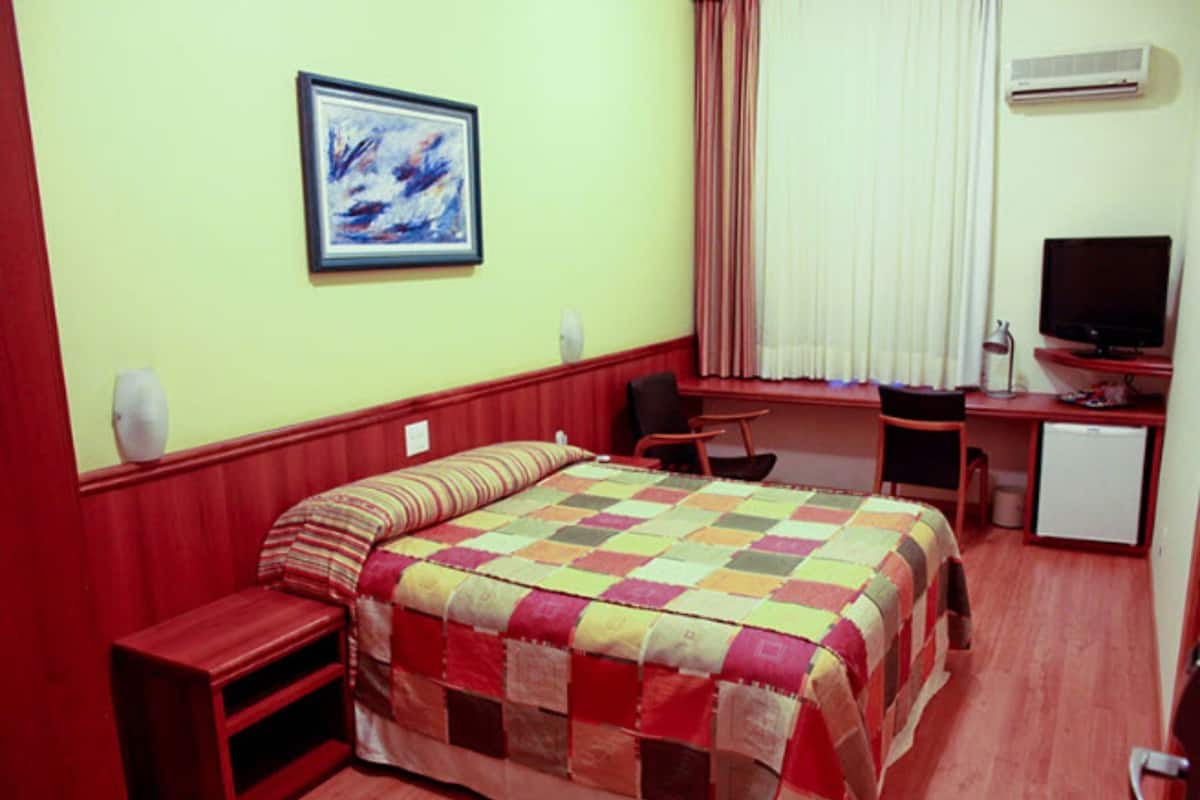 A hotel room with a bed, a desk with a computer, a television, and a small refrigerator.