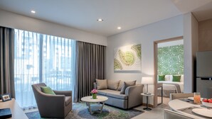 Una habitación de hotel moderna con sofá, sillón, mesa de comedor y vistas a la ciudad a través de amplias ventanas.