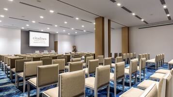A conference room with rows of beige chairs, a large screen displaying 'citadines', and a blue carpeted floor.