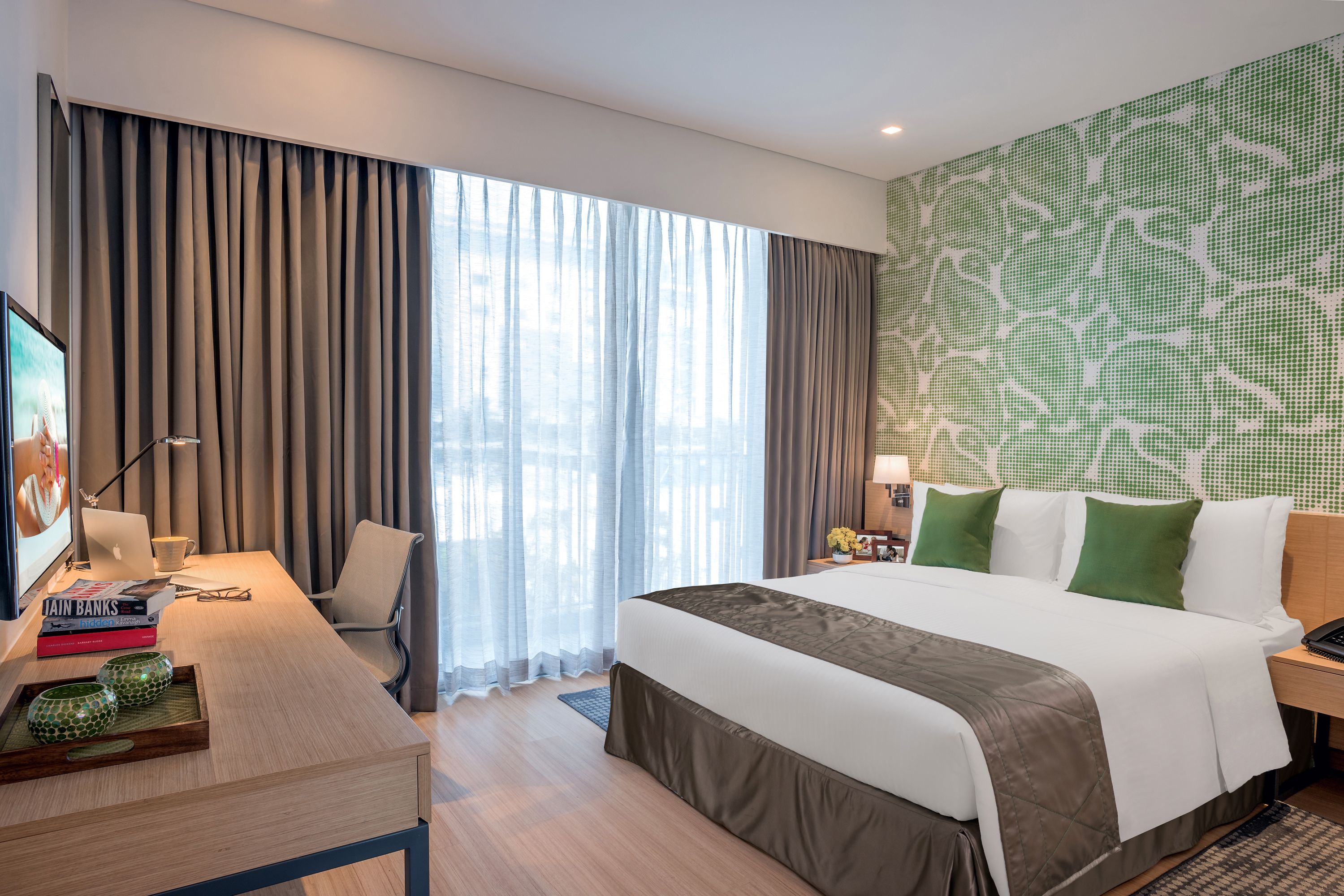 A modern hotel room with a large bed, a desk with a laptop, books, and decorative items.