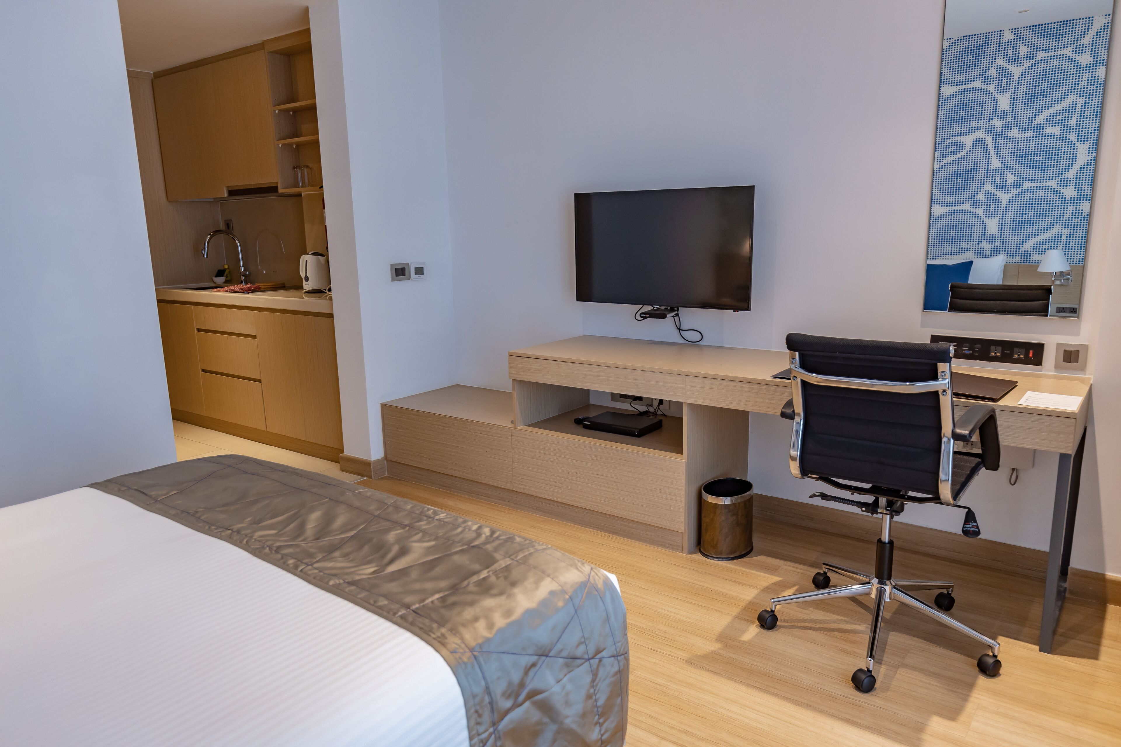 Una habitación de hotel moderna con una cama, un escritorio con computadora y silla, televisor y una zona de cocina.