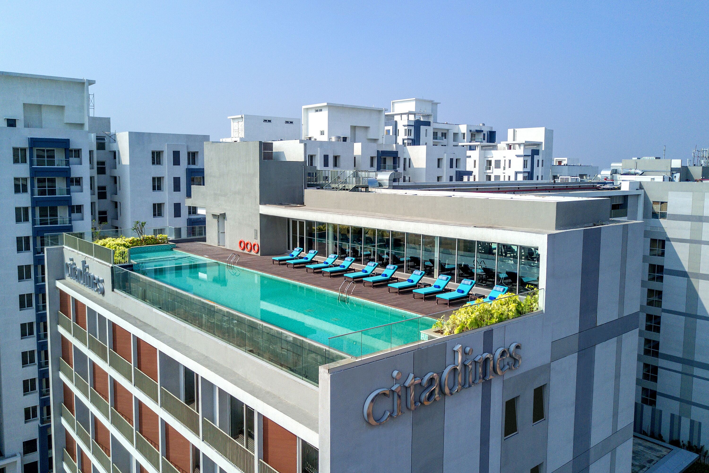 Una piscina en la azotea con sillones de descanso, barandilla de cristal y el nombre del hotel Citadines.
