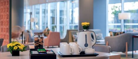 A modern dining area with a wooden table, white cups, a teapot, and a tray with cookies and a small plant.