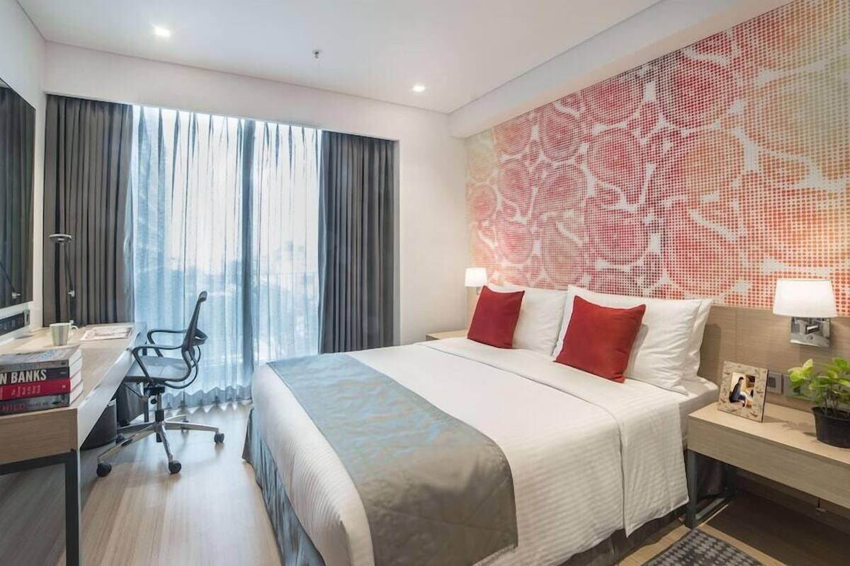 Ein Hotelzimmer mit einem großen Bett, einem Schreibtisch mit Stuhl, einem Fernseher und einem Fenster mit Vorhängen.