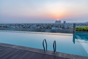 Piscina infinita en la azotea con vista a la ciudad al atardecer.