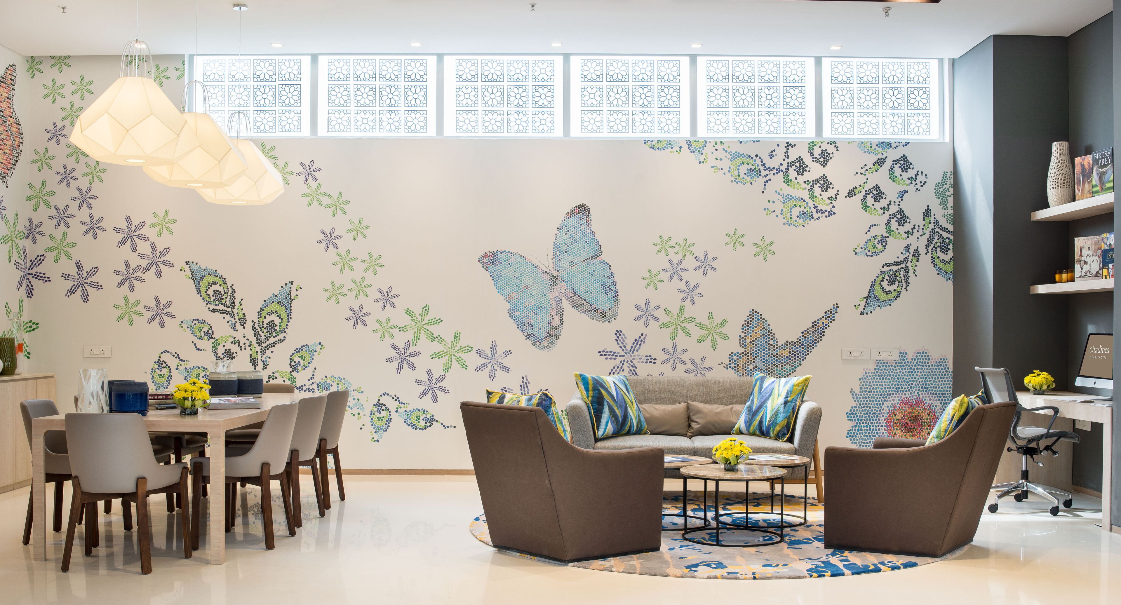 Una sala de estar moderna con comedor, que presenta un gran mural de mariposa, una mesa de centro redonda y un sofá con cojines de colores.