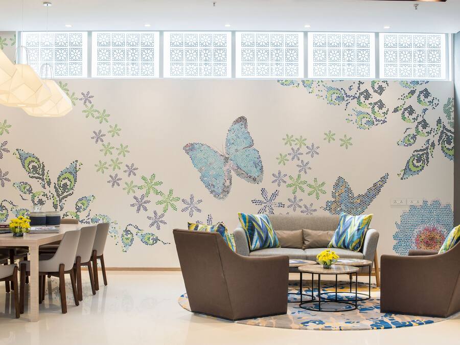 Una sala de estar moderna con comedor, que presenta un gran mural de mariposa, una mesa de centro redonda y un sofá con cojines de colores.