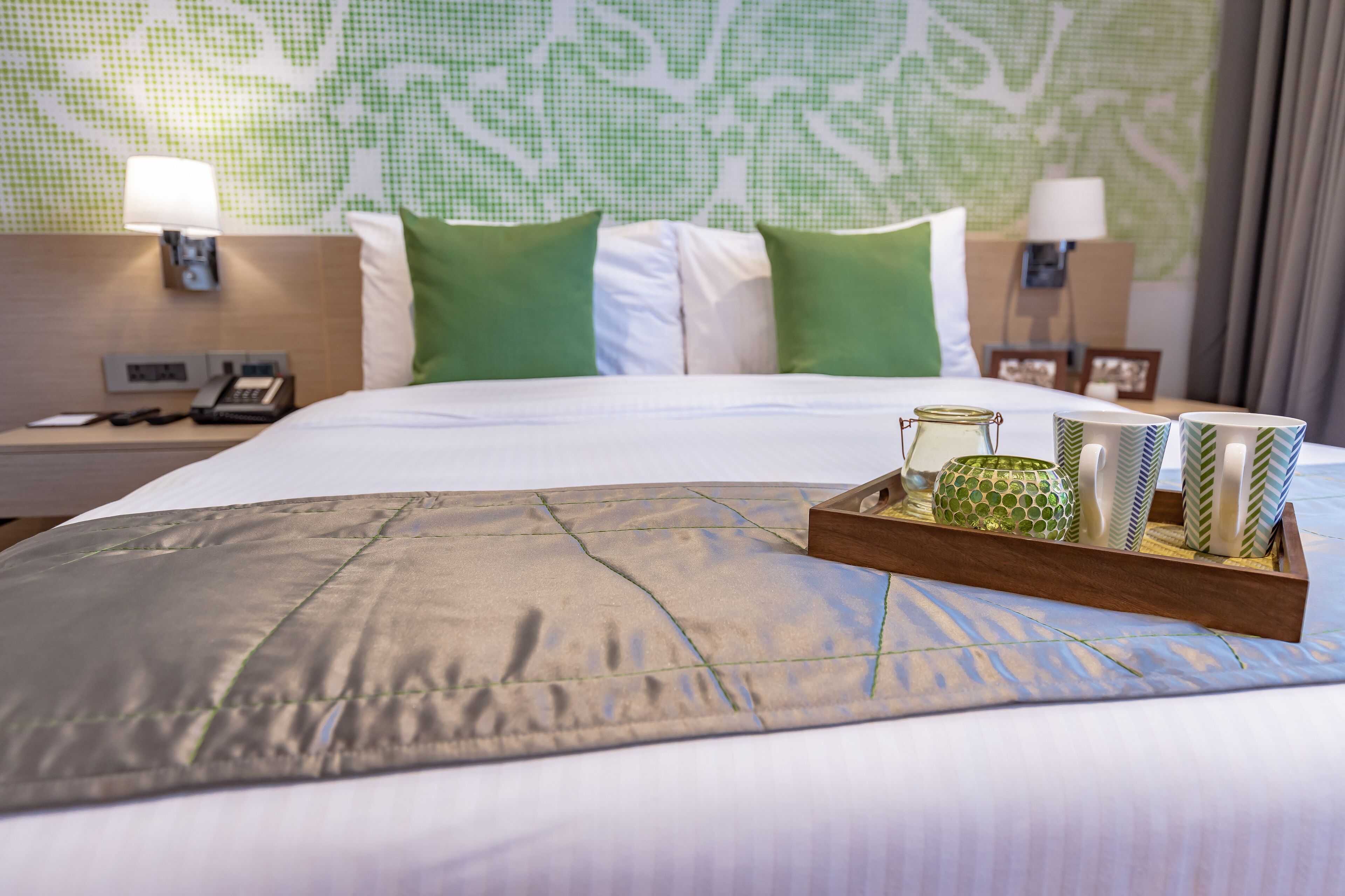A neatly made bed with a grey bedspread, green and white pillows, and a tray with decorative items.