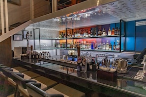 Zona de bar con asientos, una variedad de botellas, vasos y utensilios.
