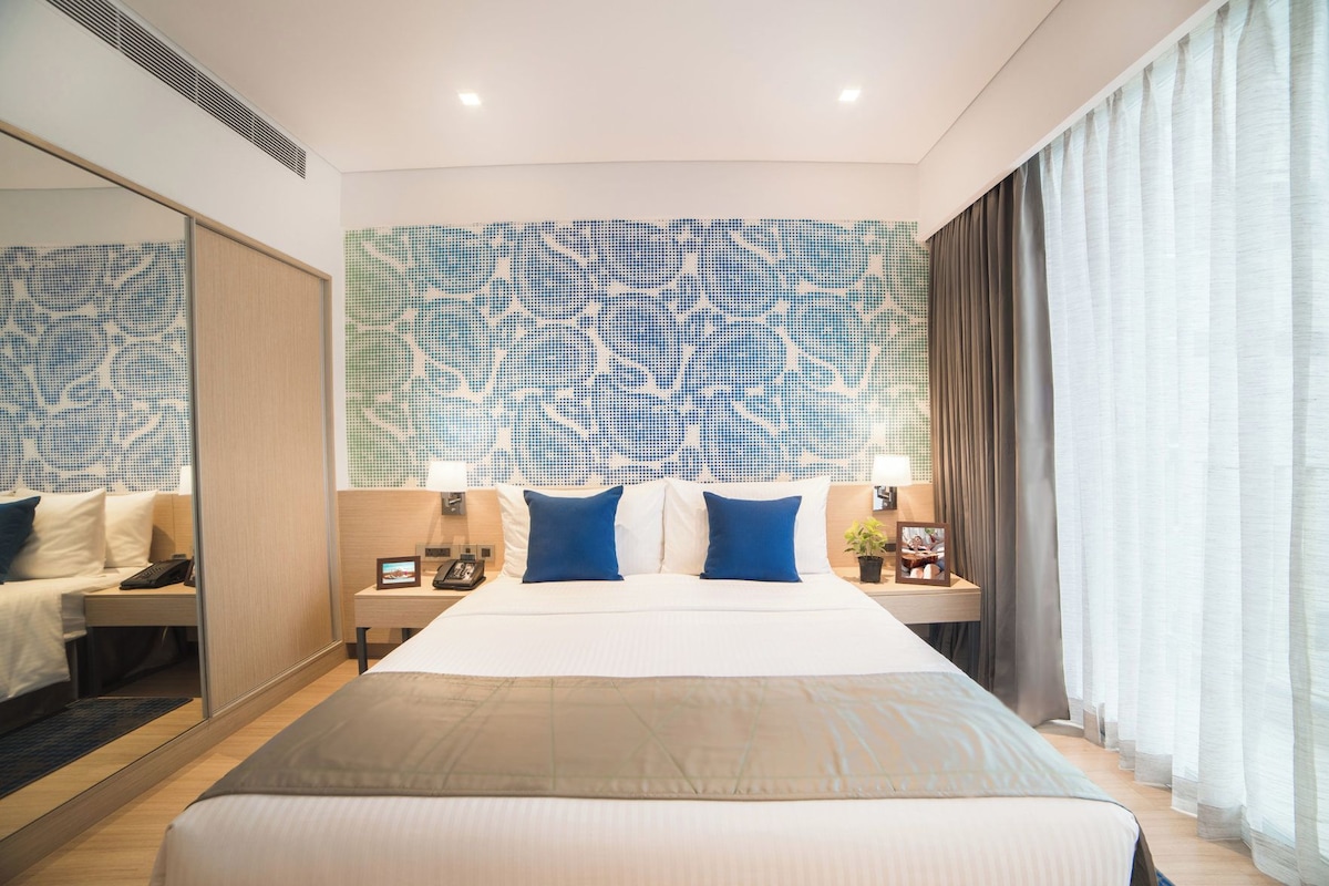 Habitación de hotel con una cama grande, dos mesitas de noche, un tocador, un espejo y una pared con diseño.