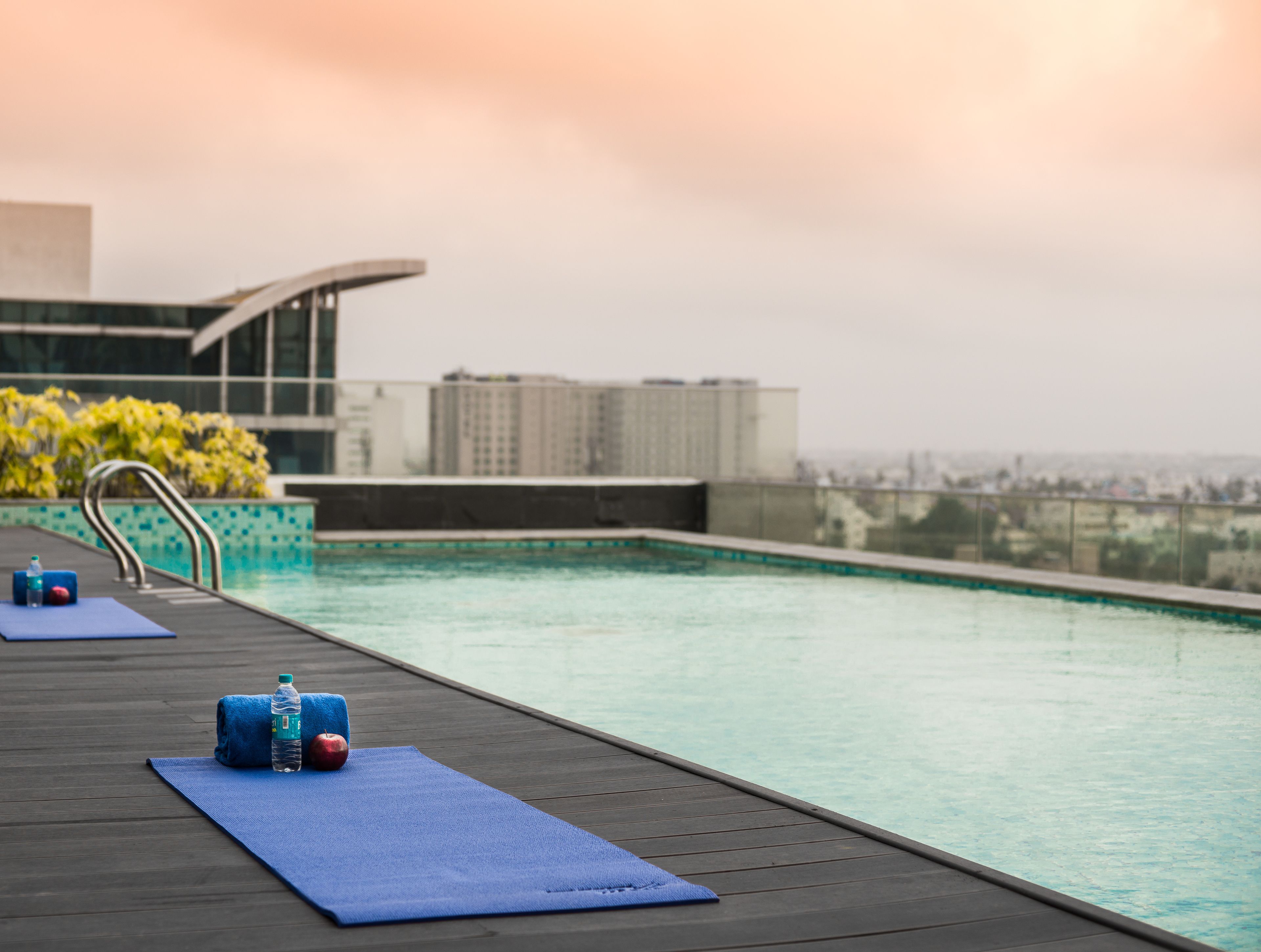Ein Pool auf dem Dach mit Yogamatte und Wasserflasche, mit Blick auf eine Stadtlandschaft.