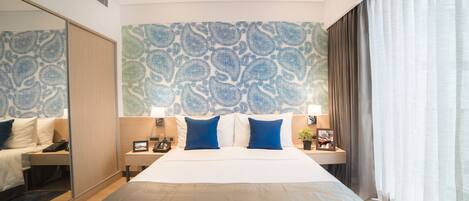 A hotel room with a large bed, a bedside table with a lamp, a nightstand with a phone, and a wall with a blue and white pattern.