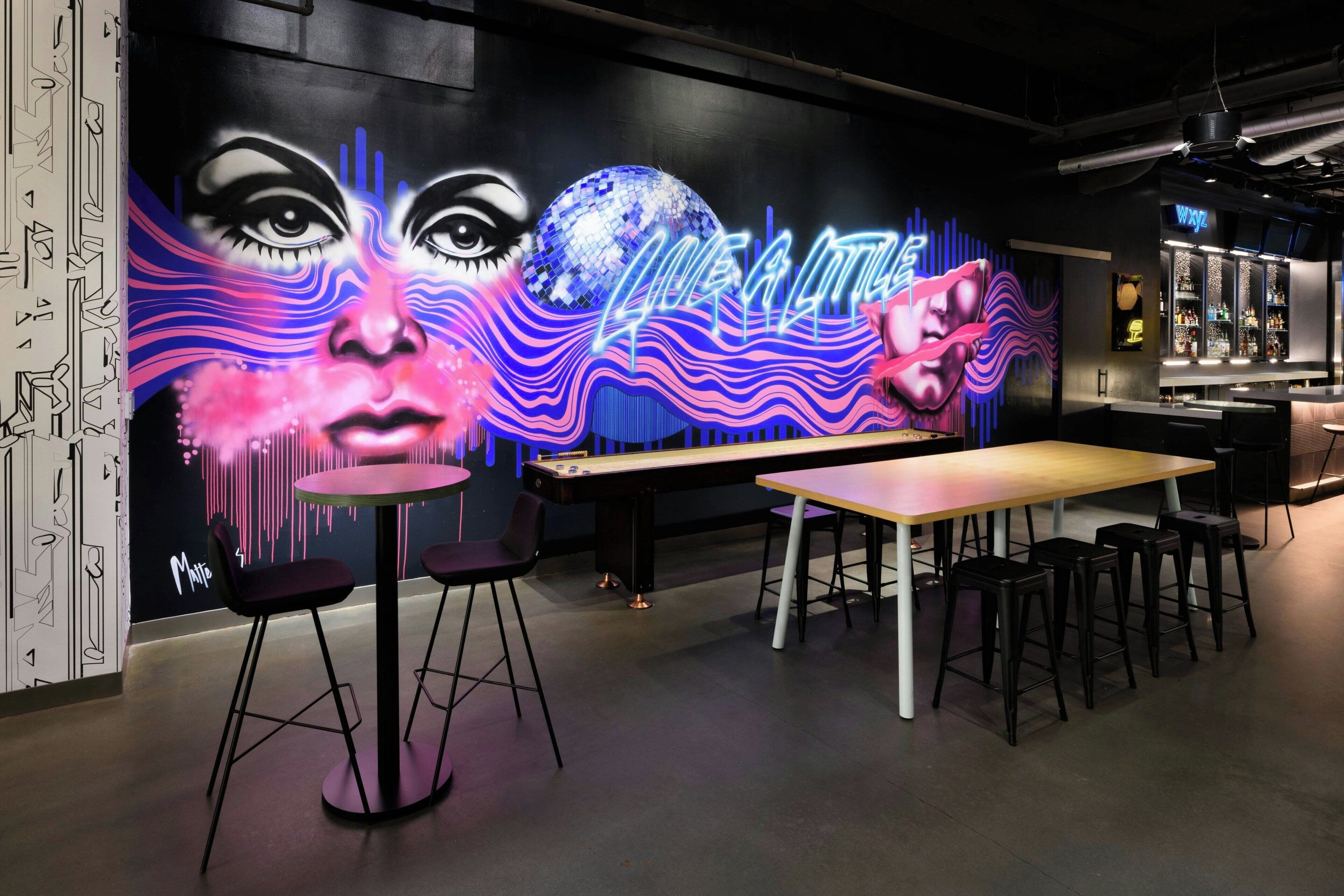 Una zona de bar con un letrero de neón, una mesa larga y varios taburetes.