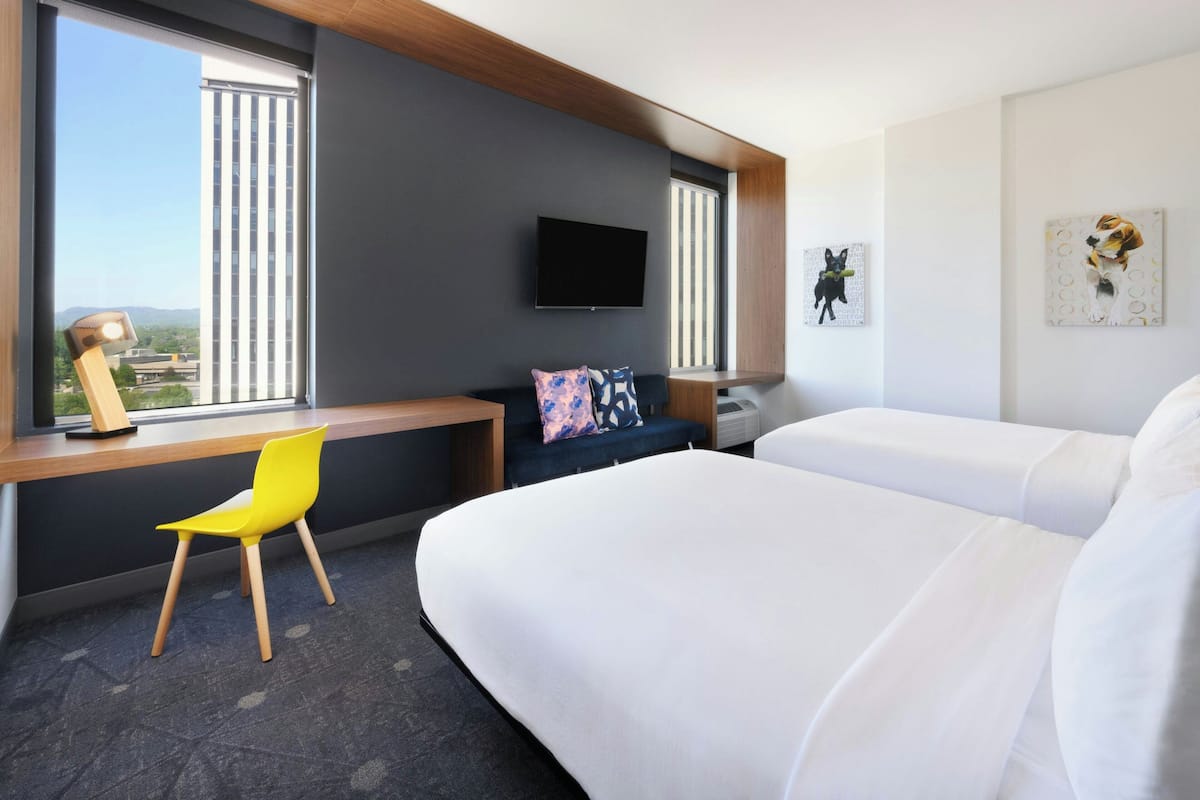 Una habitación de hotel con una cama, un escritorio con silla, televisión y obras de arte en la pared.
