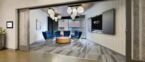 A modern conference room with a large TV screen, blue chairs, a round table, and a patterned carpet.