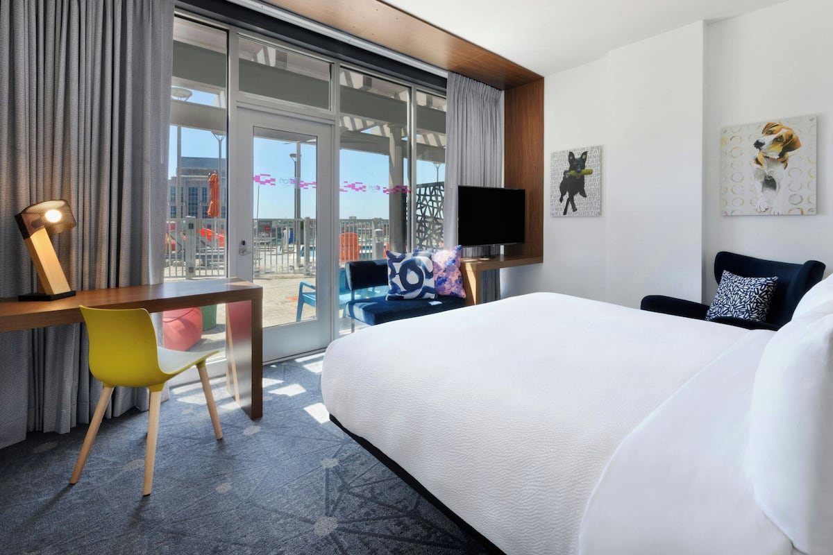 Habitación de hotel con una cama grande, un escritorio con una silla, un televisor y obras de arte en las paredes.