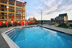 A swimming pool with lounge chairs and umbrellas, surrounded by modern buildings and a clear sky. - Aloft by Marriott Greenville Downtown (Greenville)