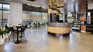 Un café moderne avec un comptoir central, plusieurs espaces pour s’asseoir et de grandes fenêtres.