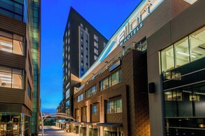 A modern hotel with a prominent 'AIO' sign, featuring a glass facade and a brick exterior. - Aloft by Marriott Greenville Downtown (Greenville)