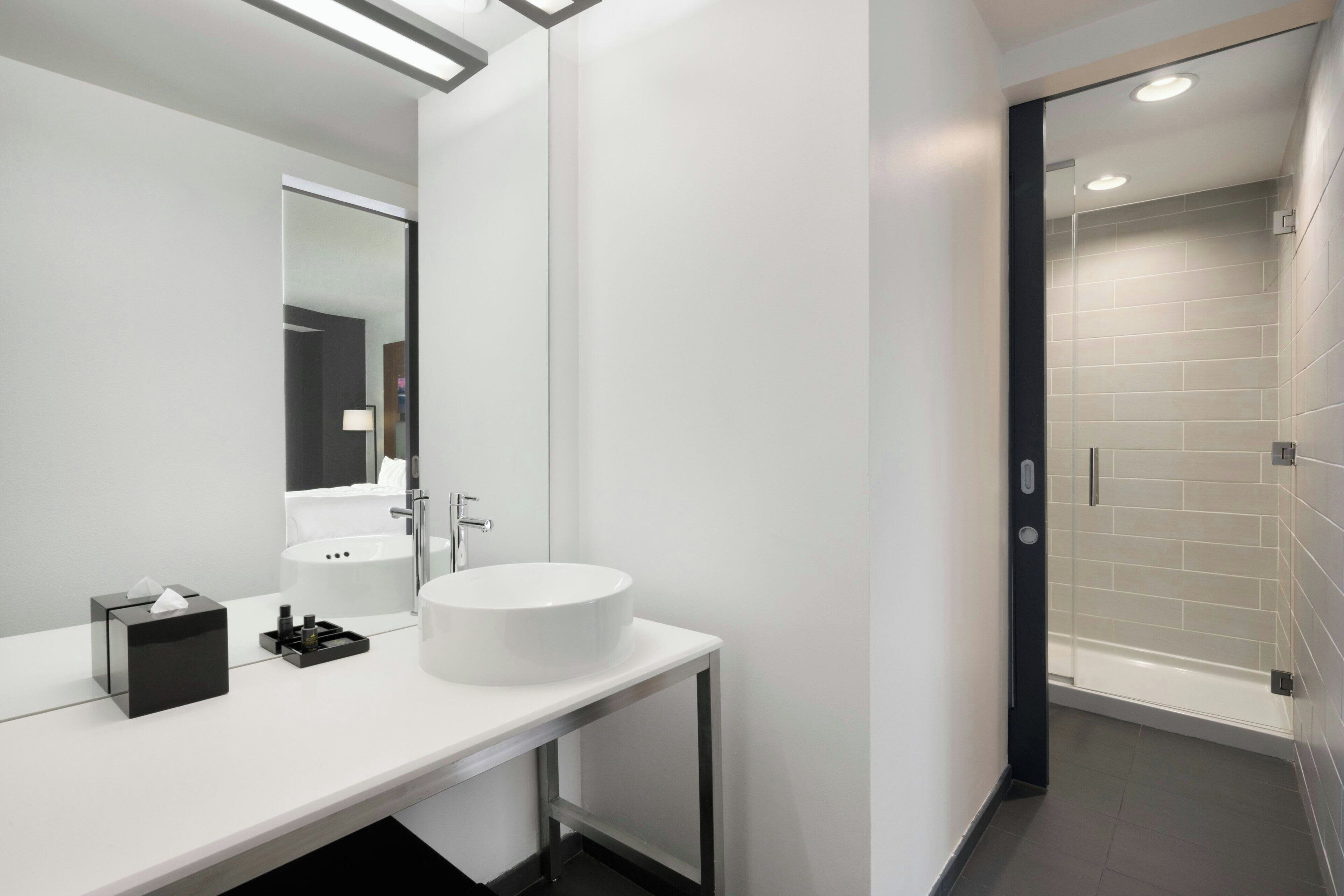 A modern bathroom with a white sink, mirror, and a glass shower enclosure.